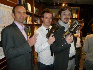 A photograph: Mark de Jager, James Long and Den Patrick hold up steampunk style guns